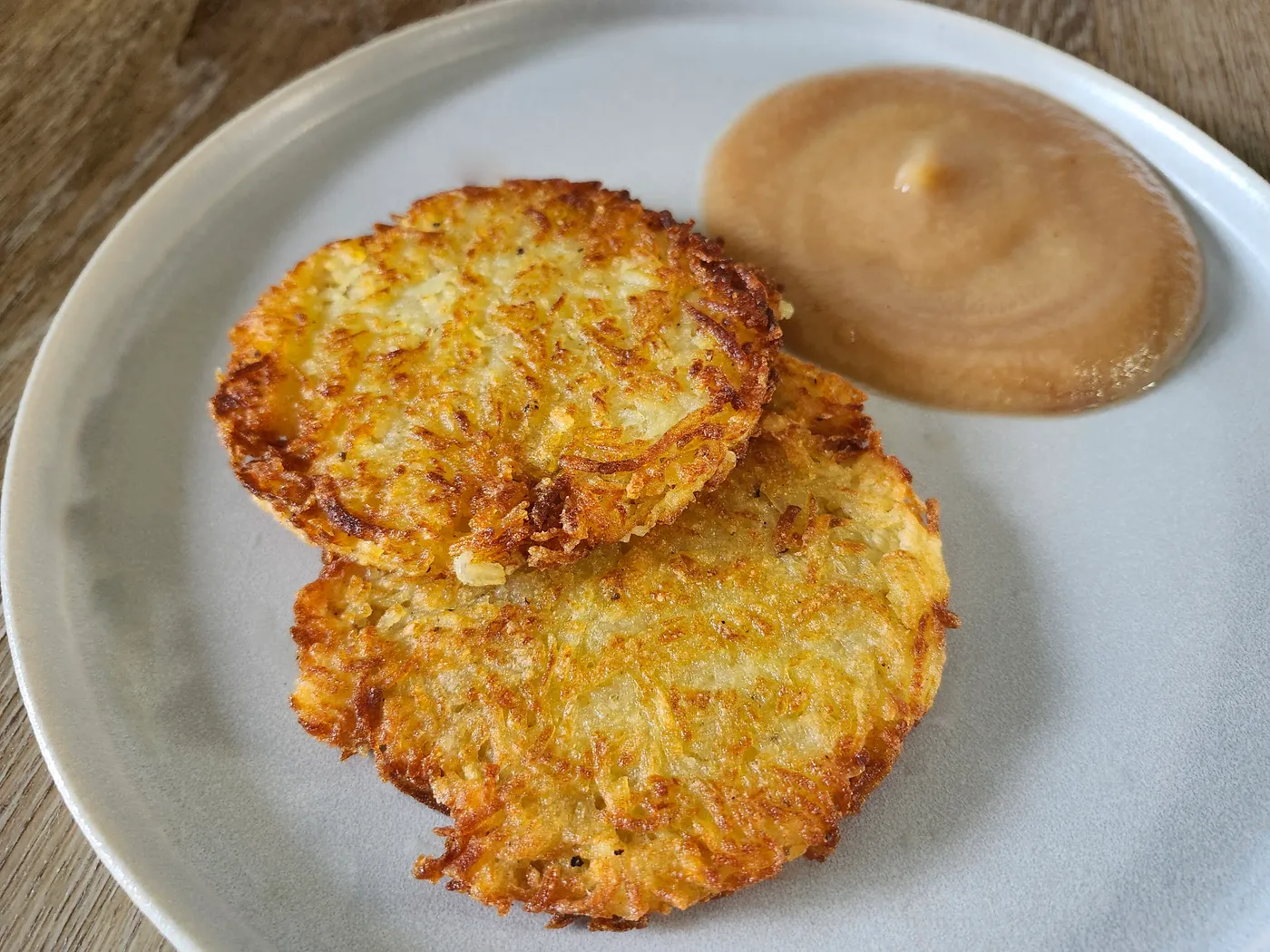 Zwei goldbraun gebratene Rösti auf einem Teller mit Apfelmus